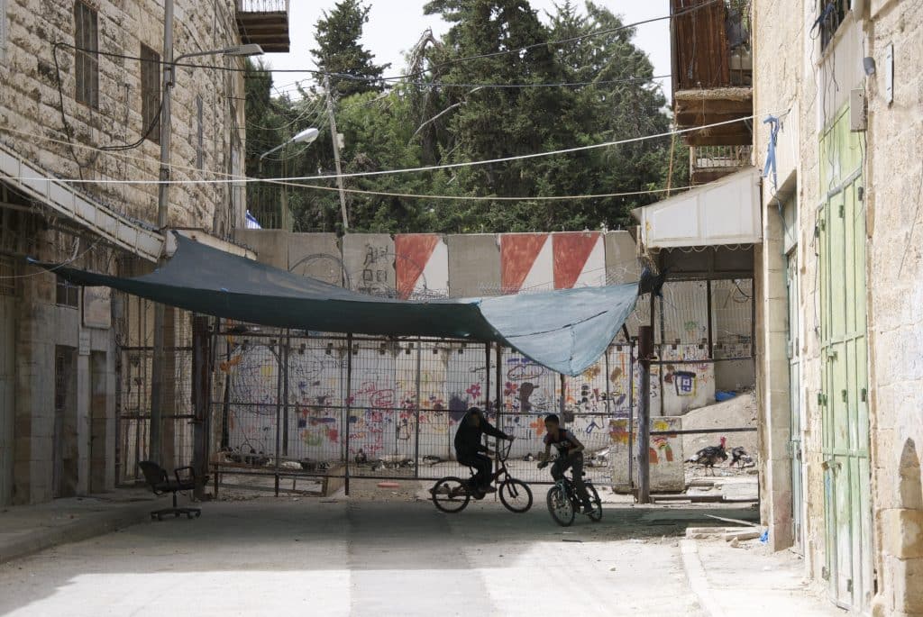 Children cycle in the gaze of Israeli soliders by the wall which cuts Hebron in two